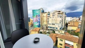 A balcony with a table and chair, overlooking a cityscape with buildings and a mountain in the distance. - Hotel Star Light Tirane (Tirana)