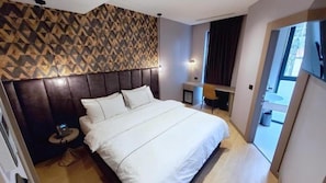 Een hotelkamer met een groot bed, een hoofdbord met een geometrisch patroon, een bureau met een stoel, en uitzicht op buiten.