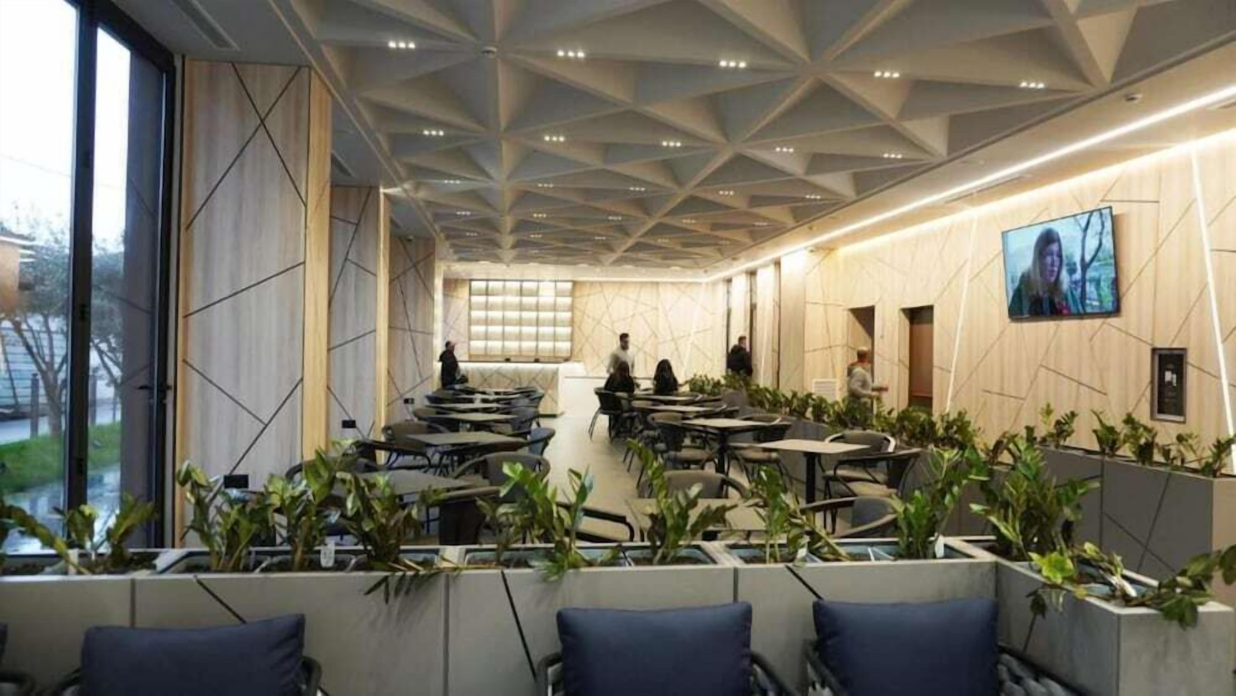Une salle de conférence moderne dotée d’un plafond au design géométrique, de tables, de chaises et de plantes en pot.