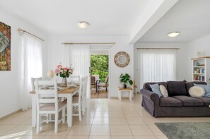 Ein geräumiger Wohnbereich mit Esstisch, weißen Stühlen, einem grauen Sofa und einem Bücherregal.