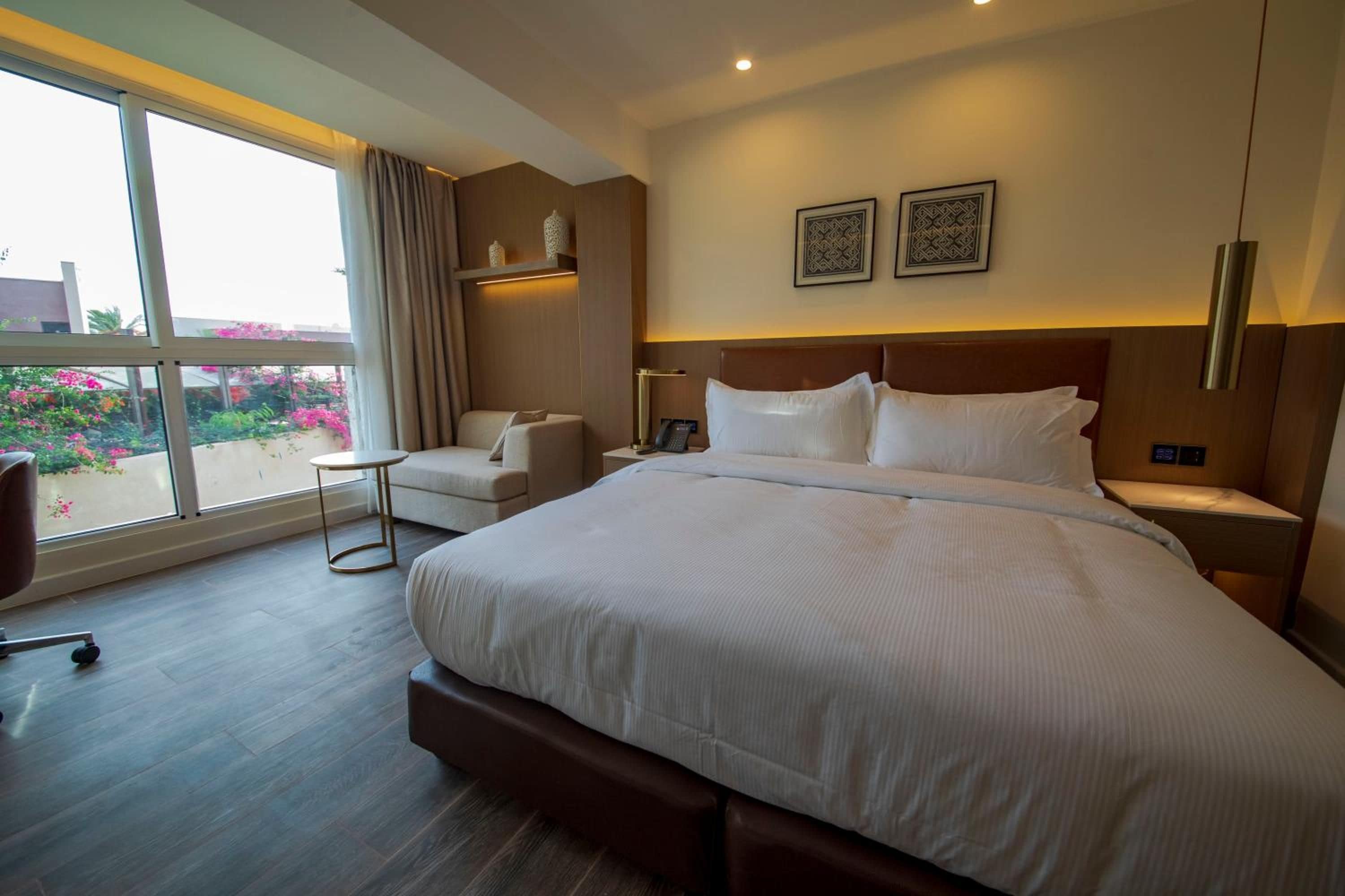 Habitación de hotel con una cama grande, un área de descanso con una silla, una mesita y vistas al exterior.