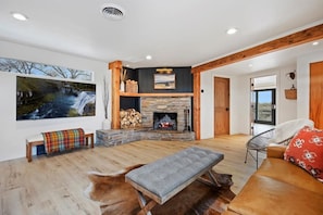 A spacious living room with a stone fireplace, wooden beams, a large window with a view, and a cozy seating area.