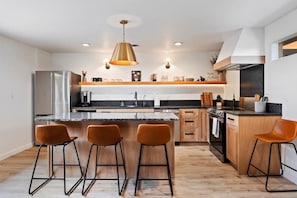 A modern kitchen with a central island, bar stools, a stainless steel refrigerator, and a built-in oven.
