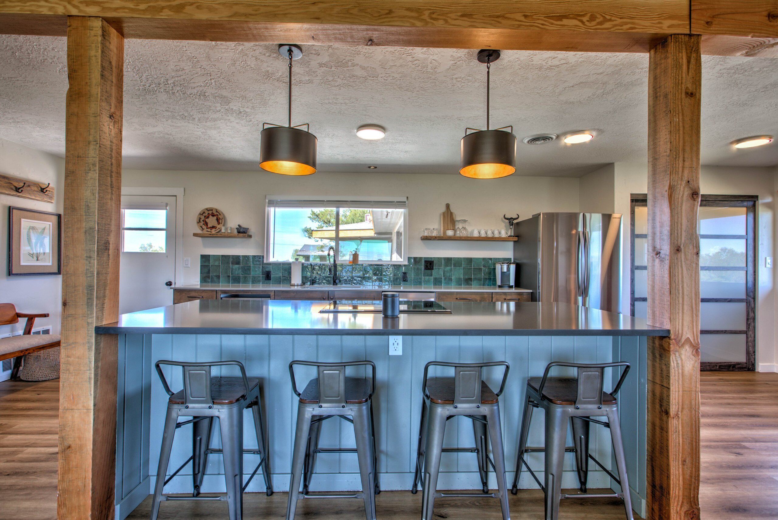 A kitchen with a central island, bar stools, pendant lights, and a stainless steel refrigerator.