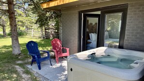 Uma banheira de hidromassagem com exterior em pedra, duas cadeiras Adirondack e uma porta de vidro que dá para um quarto.