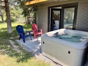 Un bain à remous avec un revêtement extérieur en pierre, deux fauteuils Adirondack et une porte vitrée donnant sur une chambre.