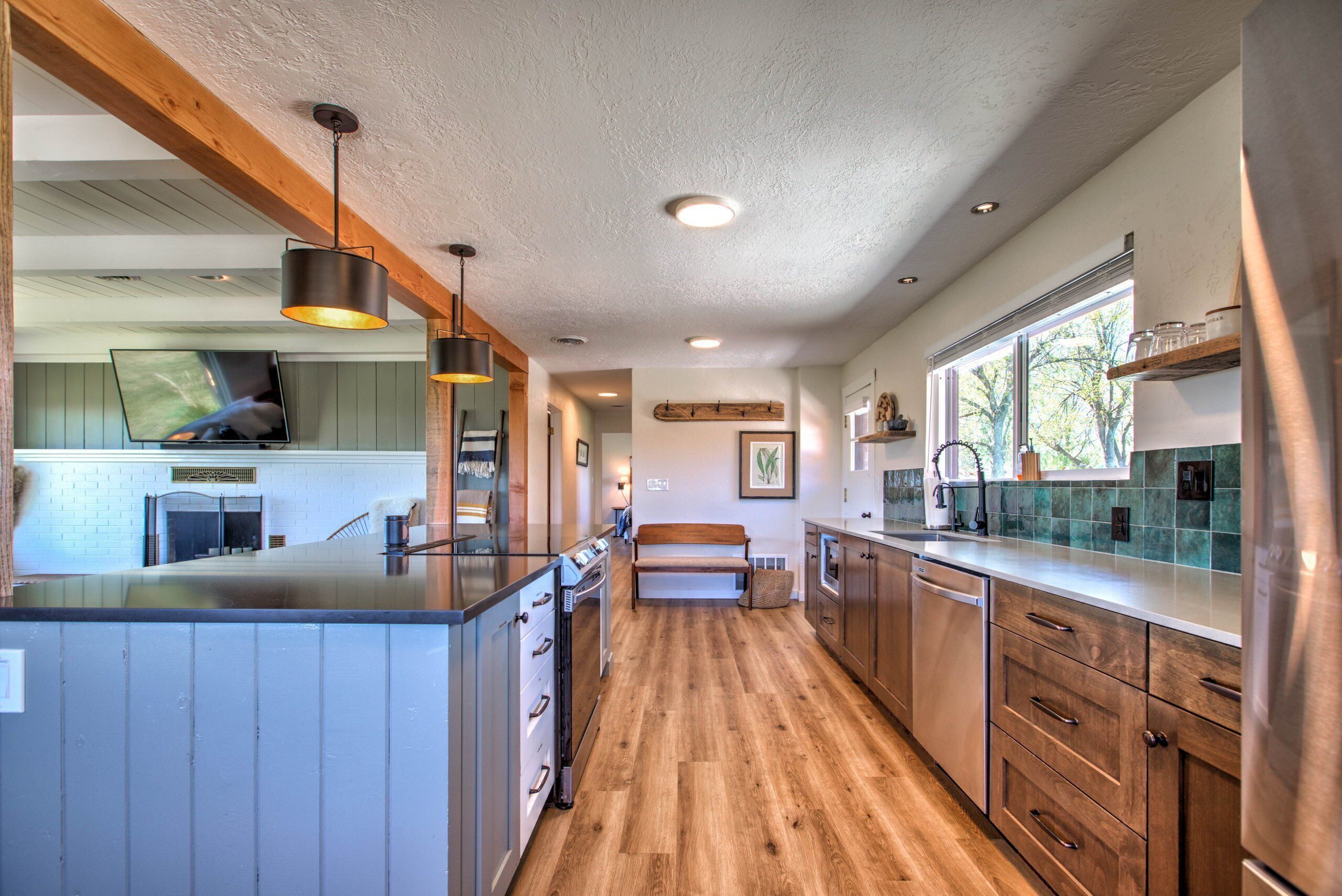 Une cuisine moderne avec des meubles en bois, un îlot central, un éclairage suspendu et une vue sur l’extérieur grâce à une grande fenêtre.