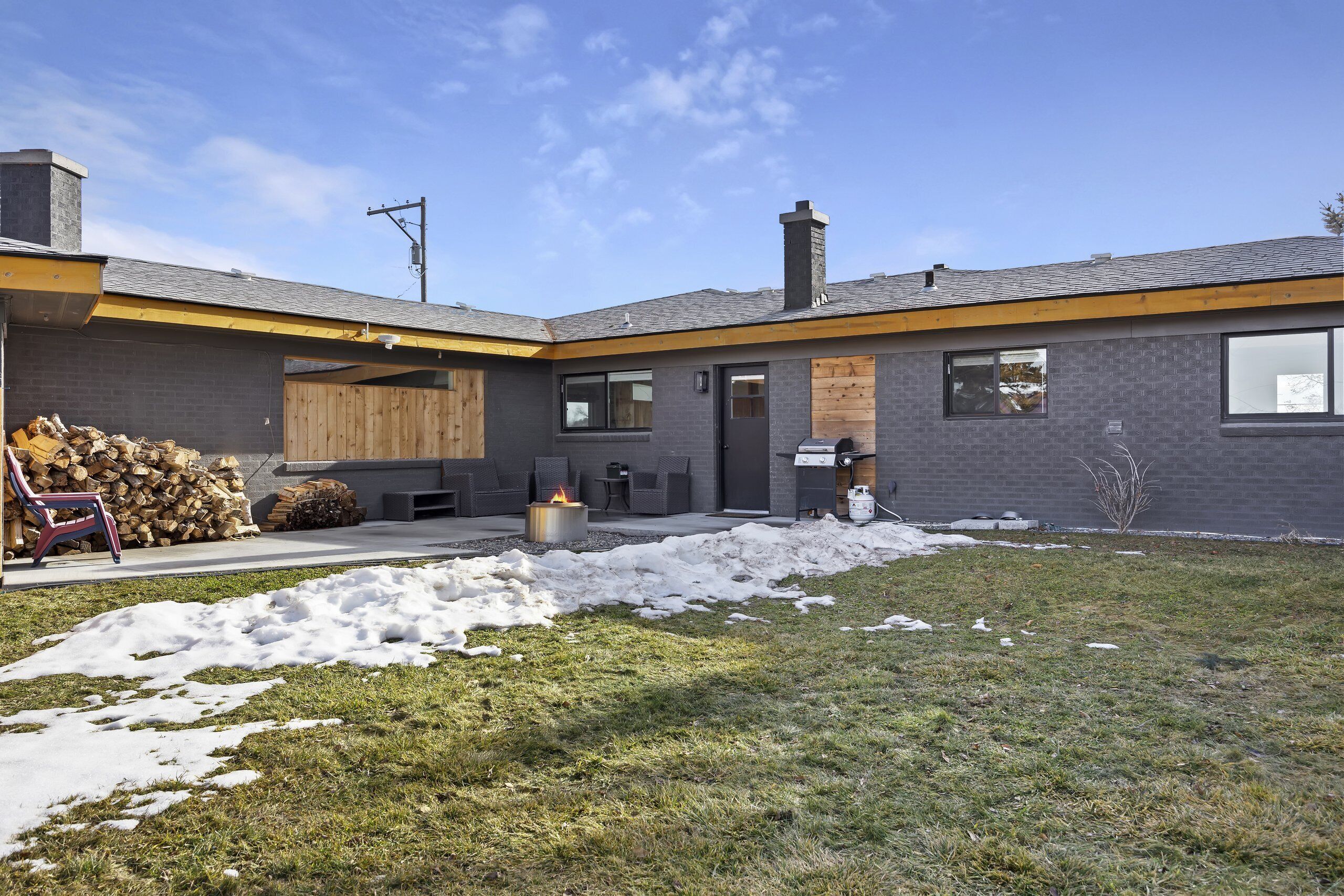 A modern house with a covered patio, a fire pit, and a stack of firewood.