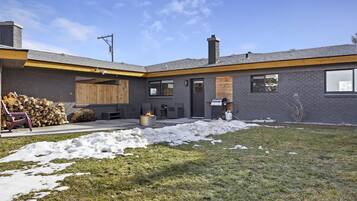 A modern house with a covered patio, a fire pit, and a stack of firewood.