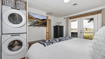 A hotel room with a bed, a washing machine, a television, and a view of the outdoors.