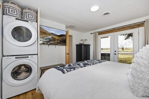 A hotel room with a bed, a washing machine, a television, and a view of the outdoors. - Rock Creek Canyon | 2BR, Hot Tub, Fire Pit, Views (Twin Falls)