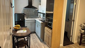 Cocina compacta con refrigerador, estufa y horno. Hay una mesa de comedor con sillas y una pequeña planta al lado.