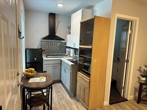 A compact kitchen with a refrigerator, stove, and oven. There is a dining table with chairs and a small plant on the side.