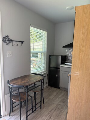 A compact kitchen with a dining table, chairs, a refrigerator, and a window with blinds.