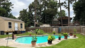 Un patio trasero con piscina, plantas en macetas, una terraza de madera y una casa.