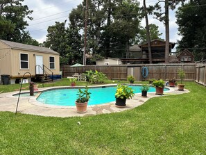 A backyard with a swimming pool, potted plants, a wooden deck, and a house. - Private tiny home oasis with pool access. (Spring)