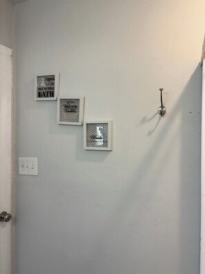 A bathroom with three framed signs on the wall, a door with a silver handle, and a light switch.