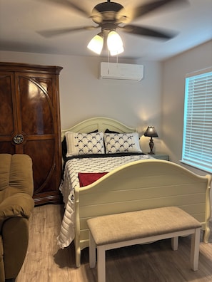 A bedroom with a bed, a bench, a wardrobe, a ceiling fan, and a window with blinds.