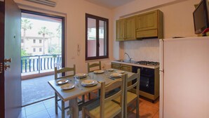Uma cozinha com uma mesa de jantar posta para quatro pessoas, fogão, geladeira e janela com vista para prédios.