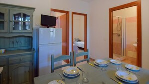 Una stanza compatta con un tavolo da pranzo apparecchiato per quattro persone, un piccolo frigorifero, un televisore sopra e un angolo doccia visibile attraverso una porta aperta.