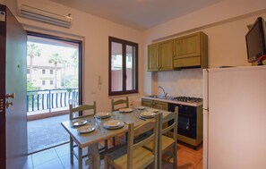 Una cocina con una mesa de comedor dispuesta para cuatro personas, una estufa, un refrigerador y una ventana con vistas a edificios.