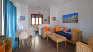 Een woonkamer met een bank, stoelen, een eettafel en een schilderij aan de muur.