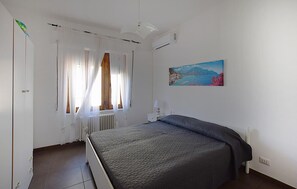 A bedroom with a bed, a radiator, a window with sheer curtains, a wall-mounted air conditioner, and a painting. - 2 bedroom gorgeous apartment in Pizzo (Pizzo)