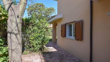 A narrow pathway leading to a building with a window and a tree on the left.