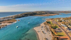 An aerial view of a coastal area with clear blue waters, boats, and a developed beachfront with buildings and roads.