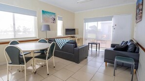 A modern living room with a dining table, sofas, a TV, and large windows.
