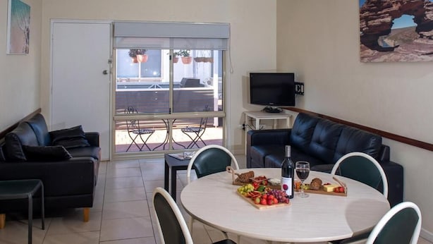 A room with a dining table set with food and drinks, a TV on a stand, a sofa, and a painting on the wall.