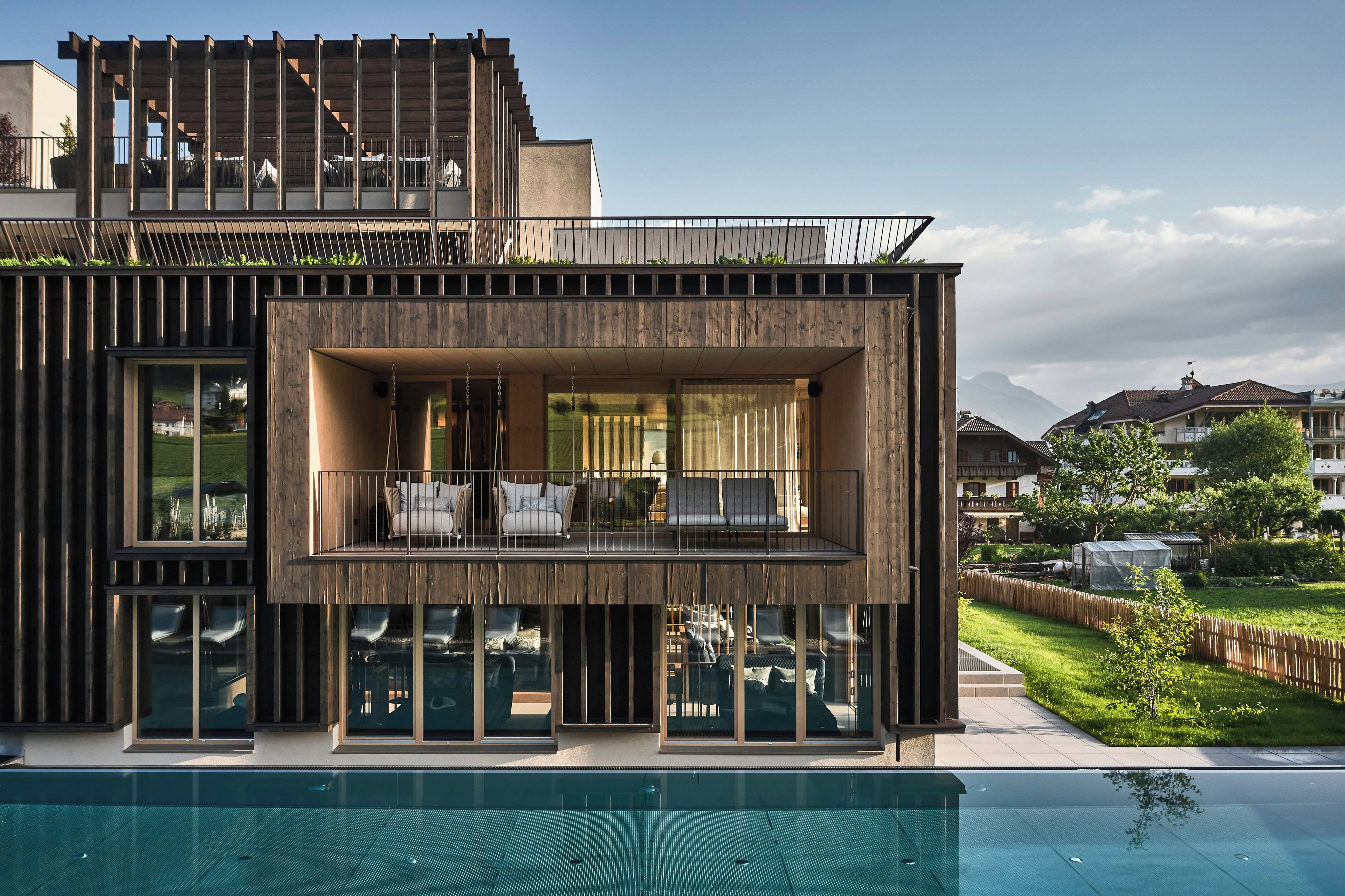 A modern house with a pool, large windows, and a balcony with outdoor seating.
