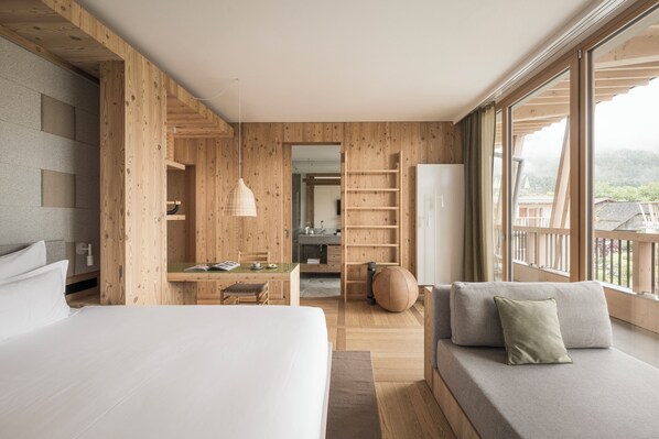 A modern hotel room with a large bed, a sofa, a dining area, and a view of the outdoors. - Falkensteiner Hotel Kronplatz (Brunico)