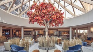A spacious lobby with a central tree, seating areas, and a high ceiling with skylights. - Falkensteiner Hotel Kronplatz (Brunico)