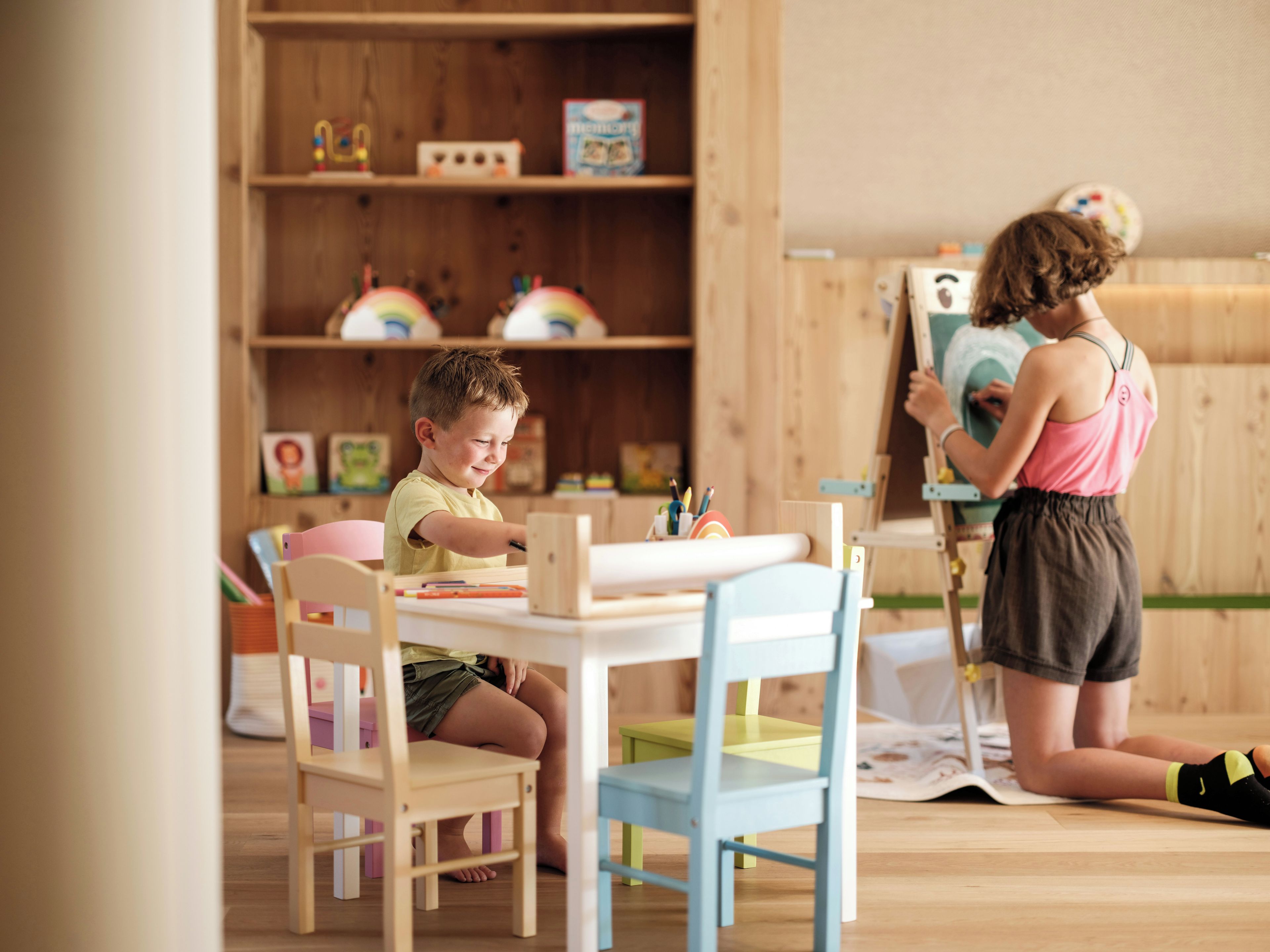 A room with a wooden floor, a table with chairs, and a bookshelf with various items.