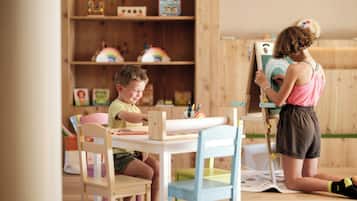 A room with a wooden floor, a table with chairs, and a bookshelf with various items.