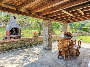 Eine Terrasse im Freien mit einem Steinkamin, einem Holztisch mit Stühlen und einer Steinwand im Hintergrund.