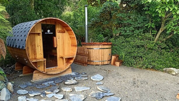 A wooden sauna structure with a door, a smaller wooden structure, and a stone pathway.