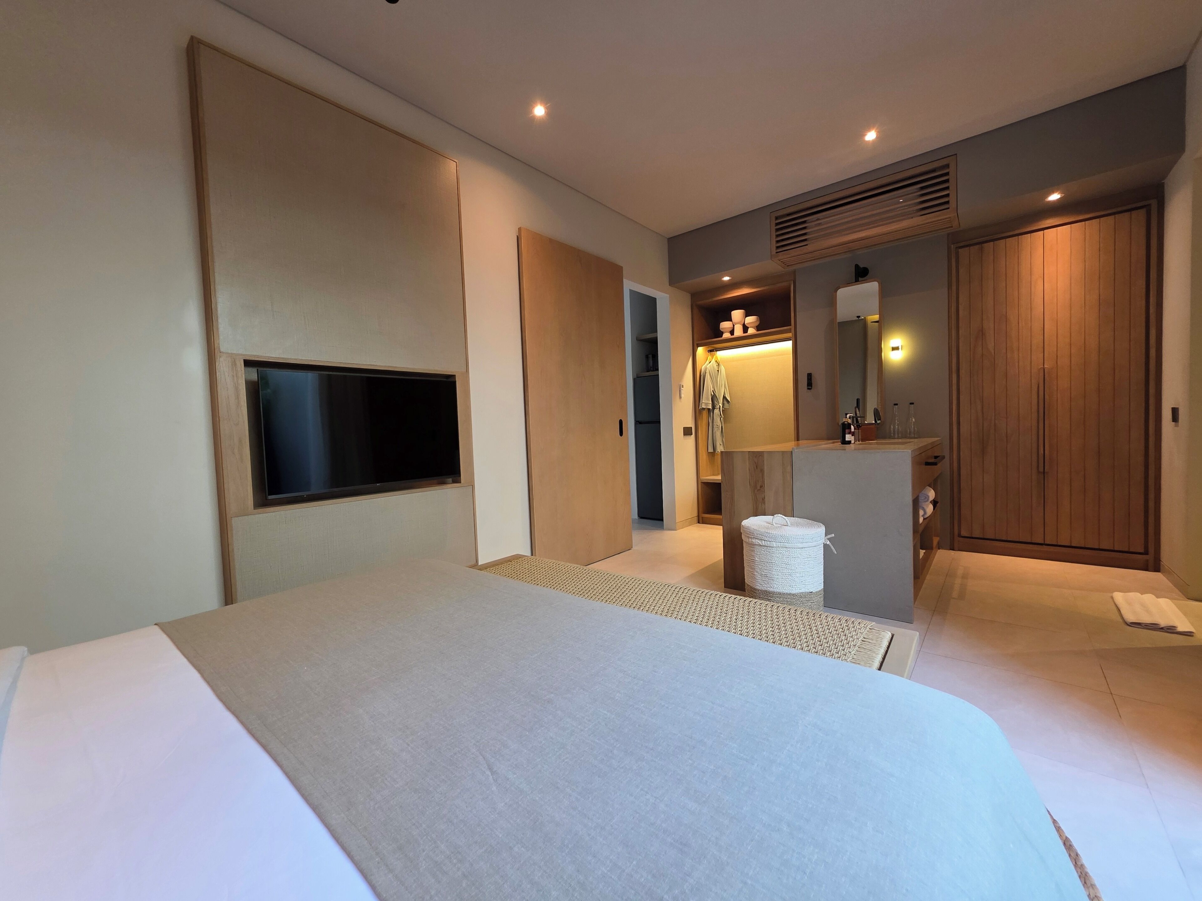 Une chambre d’hôtel moderne dotée d’un grand lit, d’un téléviseur à écran plat, d’une armoire en bois et d’une petite salle de bain.