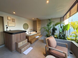 Un baño moderno con una bañera, un jacuzzi y una zona de estar con una silla y una mesita.