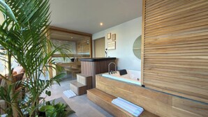 A modern spa area with a wooden reception desk, a large mirror, and a seating area with steps leading to a bathtub. - Sin Nombre Homes  (Badung)