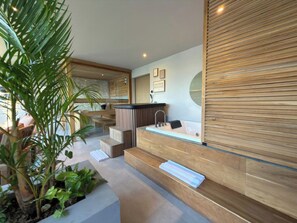 Un spa moderno con un mostrador de recepción de madera, un espejo grande y una zona de estar con escalones que conducen a una bañera.