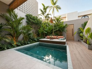 Zona de piscina moderna a l'aire lliure, amb una zona d'seients integrada, envoltada de vegetació tropical exuberanta i una pèrgola de fusta.