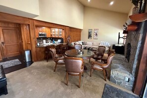 Ein Wohnzimmer mit einem runden Glastisch, umgeben von Ledersesseln, einem Steinkamin, Holzschränken und einem Sofa.