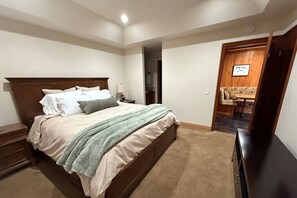 A bedroom with a bed, nightstand, and a door leading to a living area. - Updated 3BR Mammoth Condo Sleeps 9 - Walk to Ski Lift, Pool, Spa, Sauna (Mammoth Lakes)