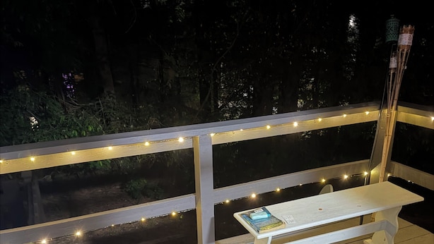 Una terraza de madera con un banco blanco y luces colgantes.