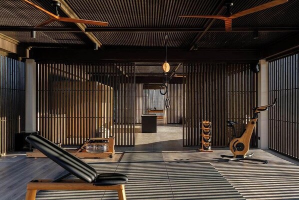 A modern interior with a tatami mat floor, a wooden bench, a stationary exercise bike, and a ceiling fan. - The Ritual, A Wellness Retreat - Adults Only (Kos)
