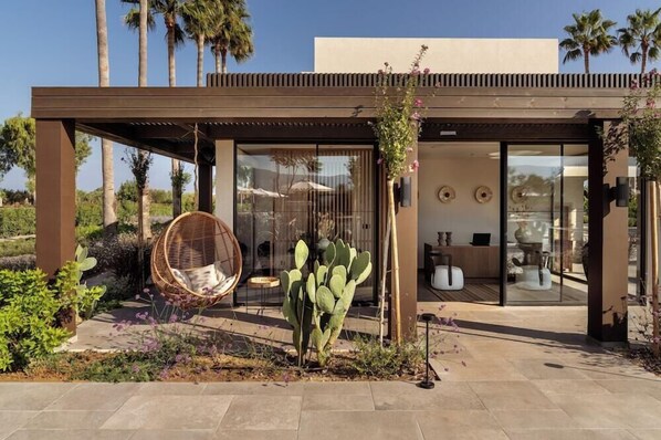 A modern building with a glass entrance, a hanging chair, and a cactus in the foreground. - The Ritual, A Wellness Retreat - Adults Only (Kos)