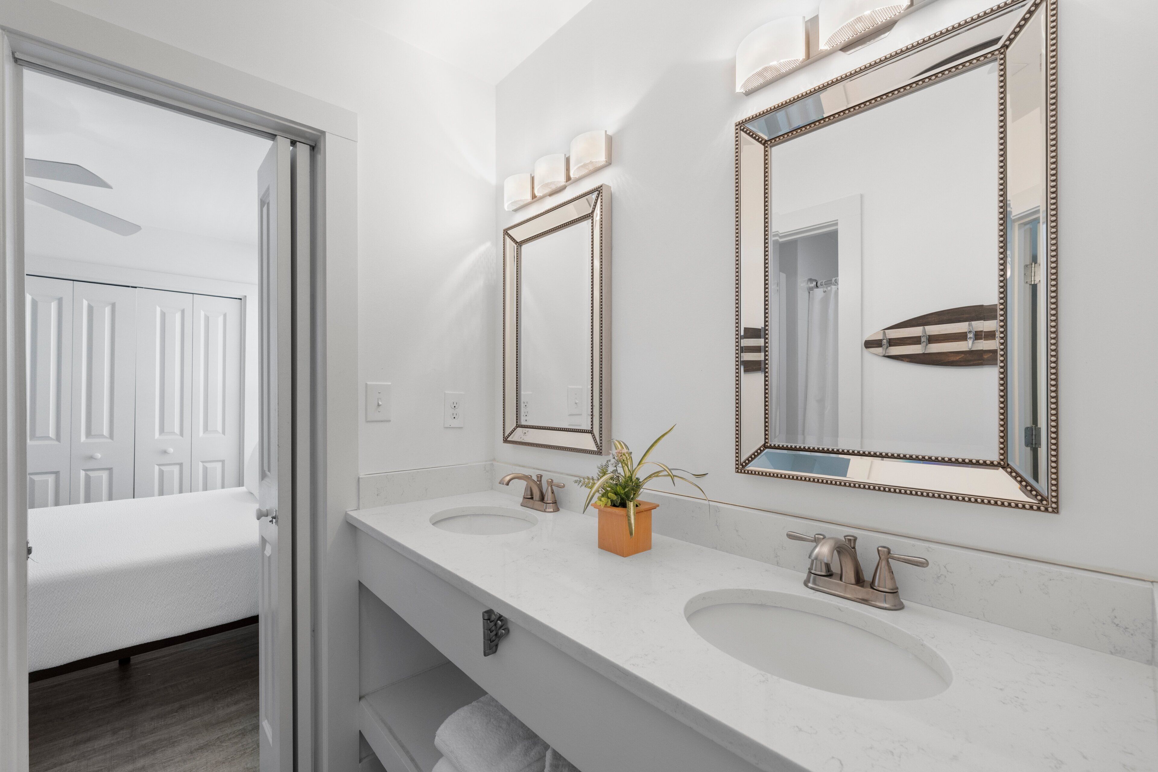 A modern bathroom with two sinks, a mirror, and a potted plant.