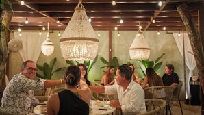 Comedor interior con mobiliario de mimbre, candelabros de cristal colgantes y un fondo de plantas tropicales.